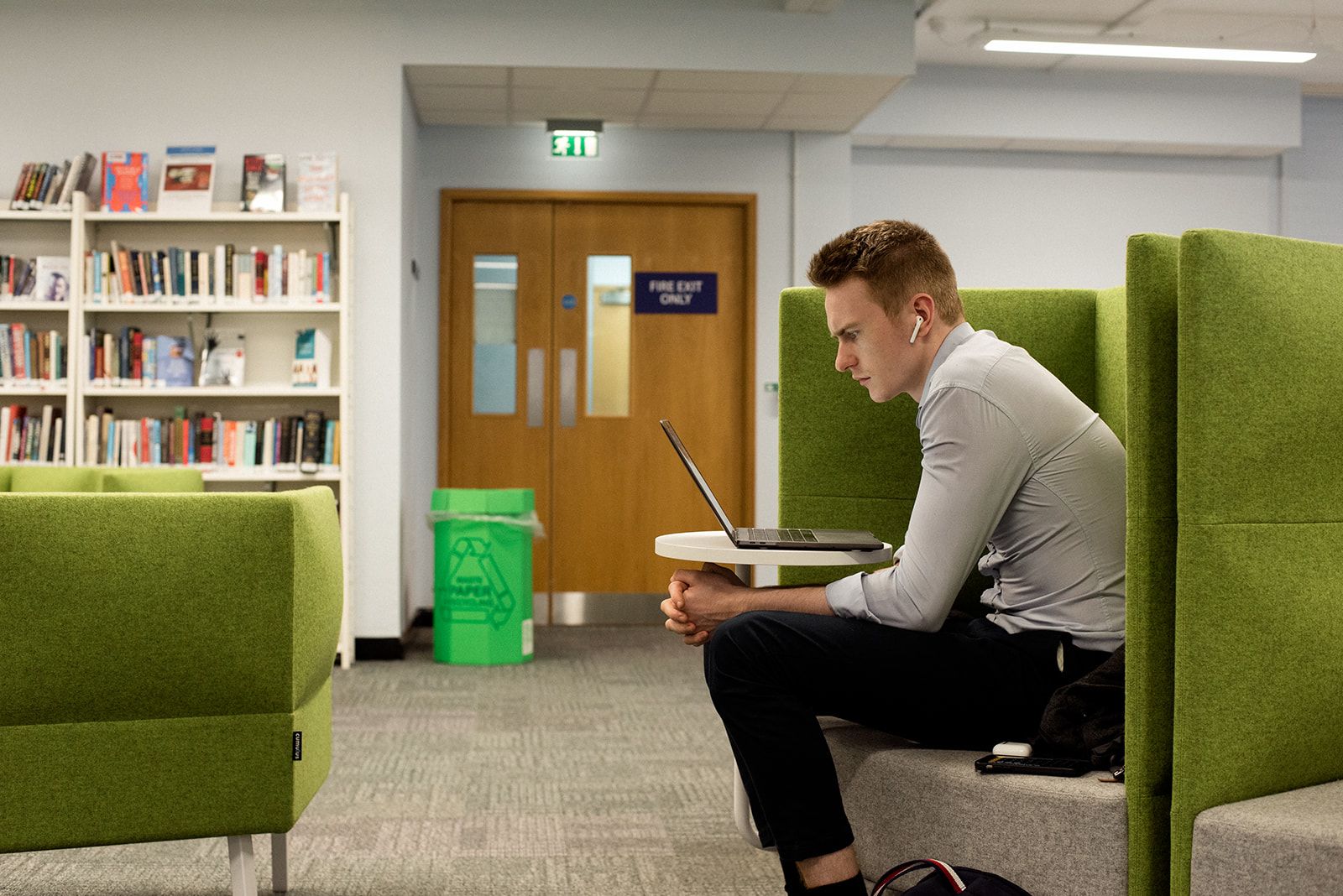 A researcher reads from a laptop whilst sitting in a green chair in the Medical Library